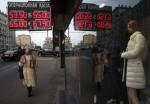 People walk along a street past a board showing currency exchange rates in Moscow