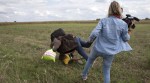 A migrant carrying a child falls after tripping on TV camerawoman (R) Petra Laszlo while trying to escape from a collection point in Roszke village, Hungary, September 8, 2015. Laszlo, a camerawoman for a private television channel in Hungary, was fired late on Tuesday after videos of her kicking and tripping up migrants fleeing police, including a man carrying a child, spread in the media and on the internet. REUTERS/Marko Djurica - RTX1RP8Z